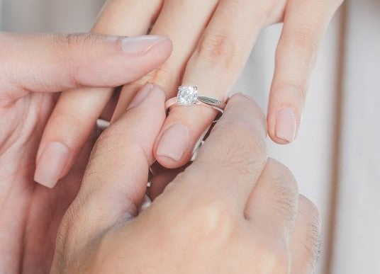 Man placing engagement ring on a woman's hand.
