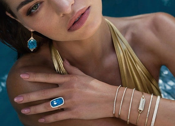 Woman in swimming pool wearing multiple gold bracelets, blue stone earrings and ring